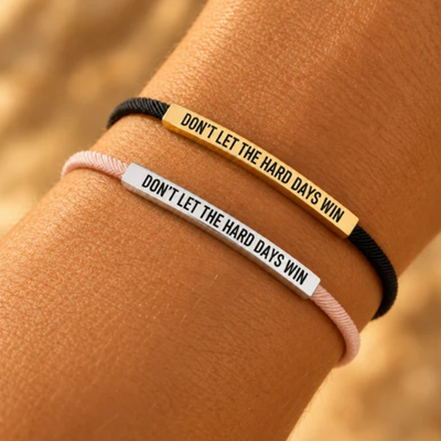 Dos pulseras «Don't Let The Hard Days Win» en la muñeca: negro y dorado, y rosa y plateado